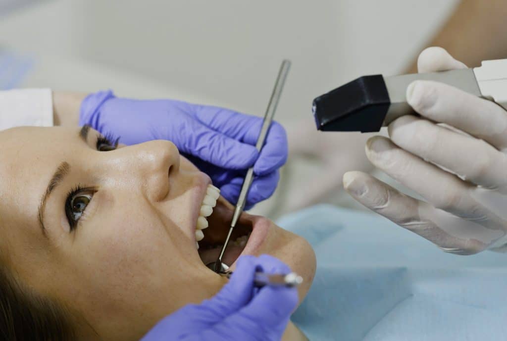 Dentista aplicando un tratamiento de anestesia dental mientras utiliza una lámpara de fotopolimerización en la boca de la paciente.