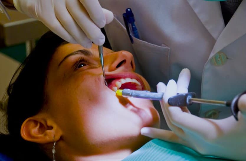 Odontóloga realizando un curetaje dental a una paciente, limpiando encías y dientes con instrumentos especializados bajo luz clínica.