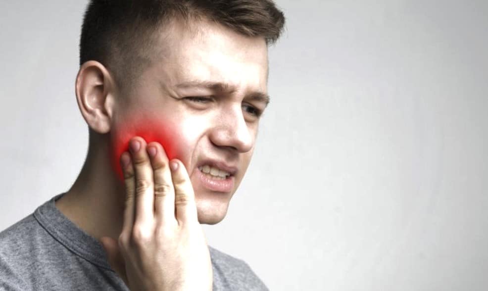 A man grimacing while holding his jaw, clearly experiencing pain from a toothache.