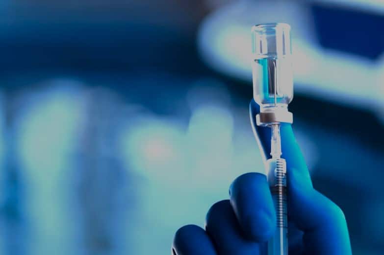 Mano con guante sosteniendo una jeringa con vial de anestesia en un entorno clínico.