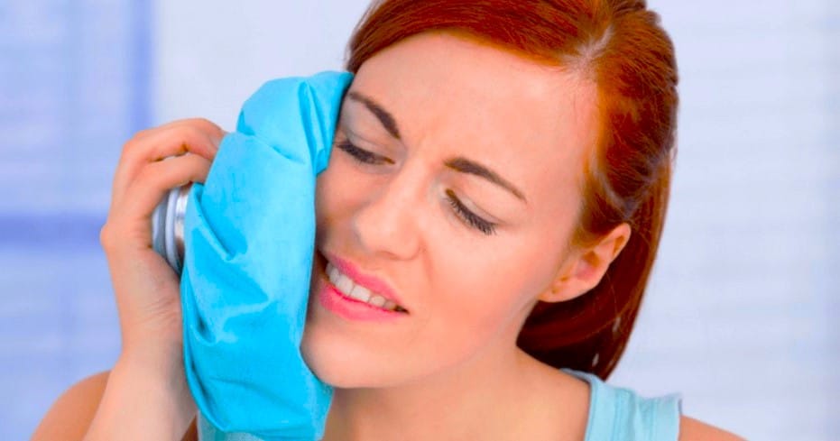 Persona sosteniendo una bolsa de hielo en la mejilla, experimentando dolor después de una extracción de muela del juicio.