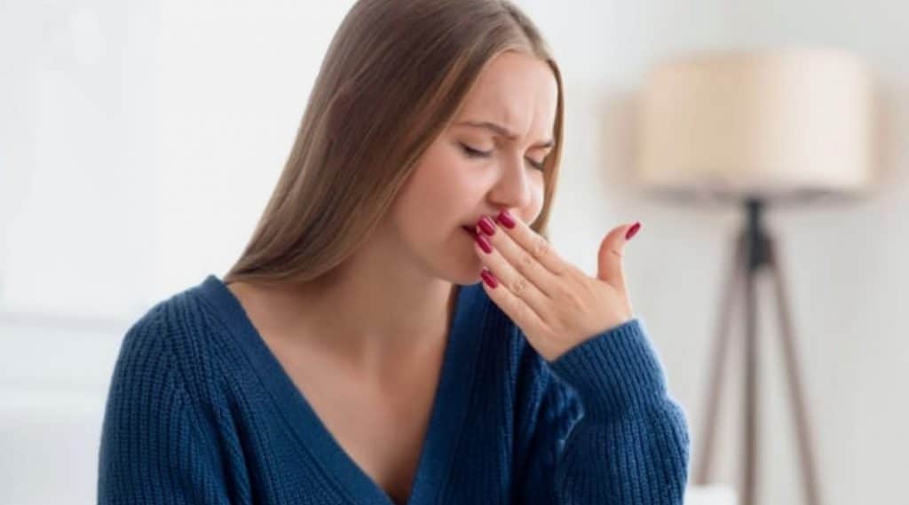 Persona con expresión de cansancio y malestar por sabor metálico en la boca.